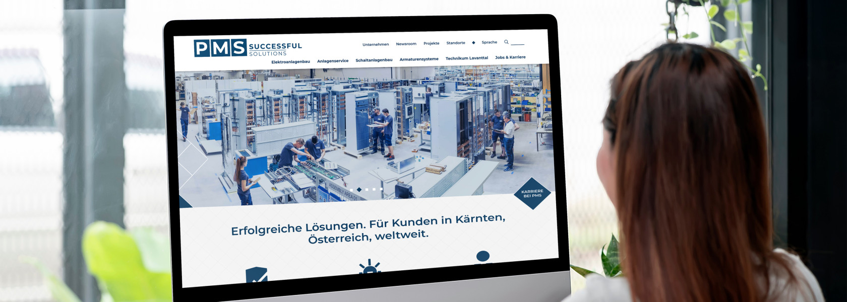 Eine Frau die vor einem großem Monitor sitzt auf dem ein Ausschnitt der PMS Website zu sehen ist.