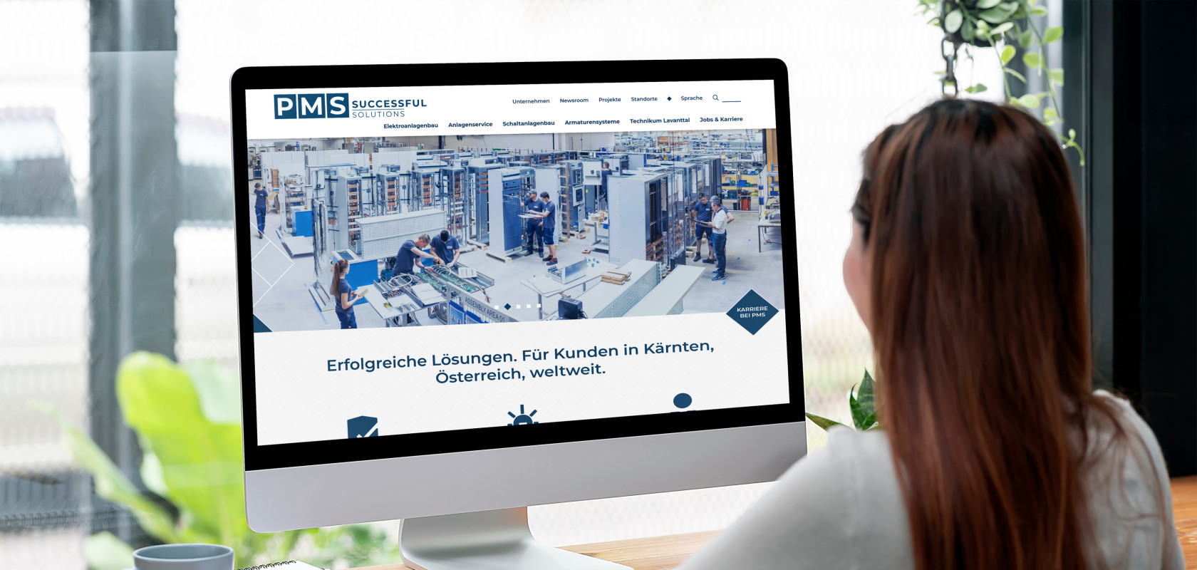 Eine Frau die vor einem großem Monitor sitzt auf dem ein Ausschnitt der PMS Website zu sehen ist.