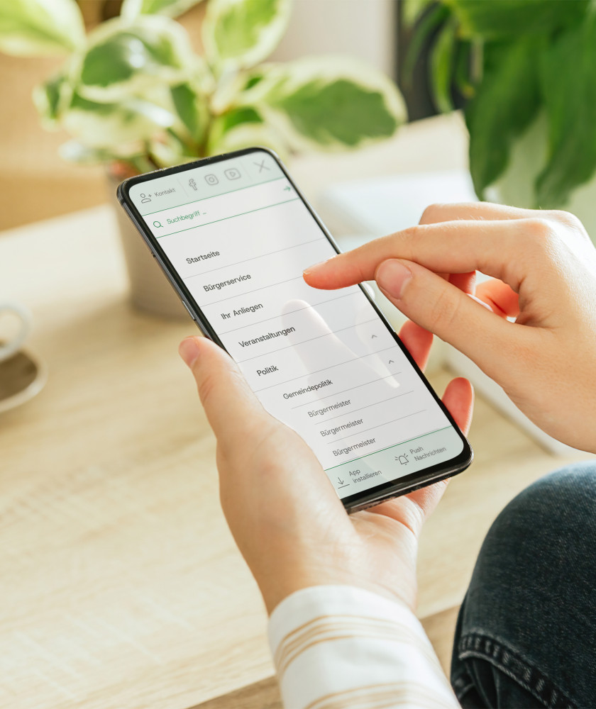 In der Hand wird ein Smarthpone gehalten, welches einen Ausschnitt des neuen Gemeindeportal Designs zeigt.