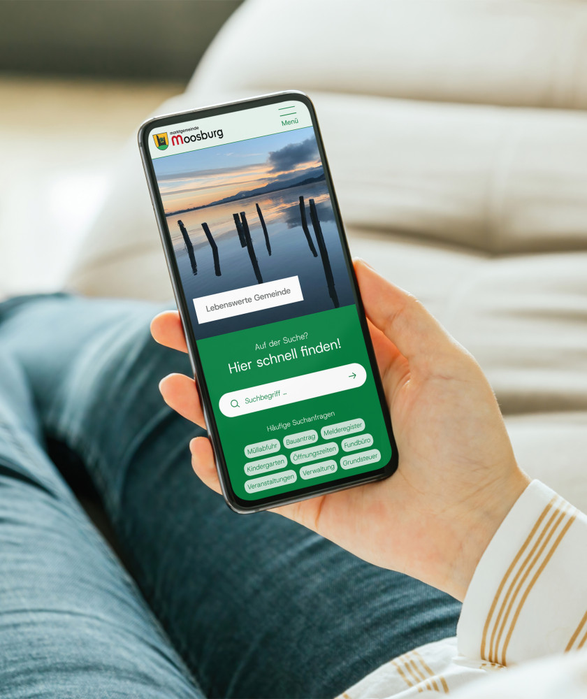In der Hand wird ein Smarthpone gehalten, welches einen Ausschnitt des neuen Gemeindeportal Designs zeigt.